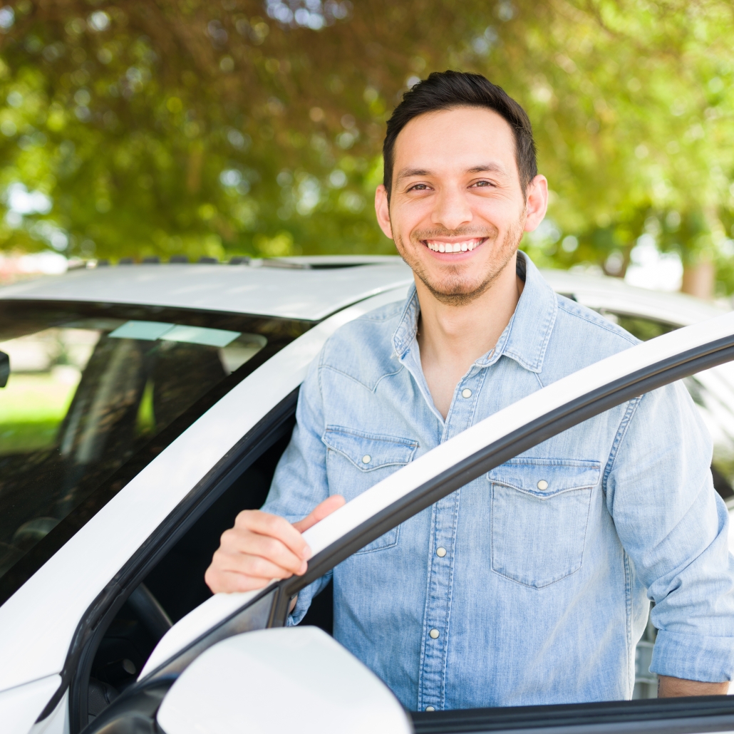 Smiling young man stands beside a car that has the driver's side door open.